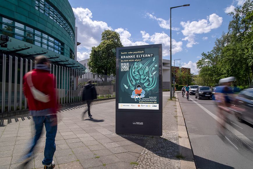 Digitale Werbesäule in einer städtischen Umgebung zeigt ein Plakat der Kampagne für Kinder kranker Eltern